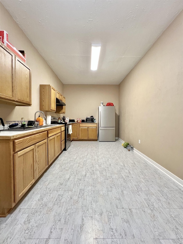 kitchen featuring light countertops, appliances with stainless steel finishes, under cabinet range hood, baseboards, and light wood-style floors