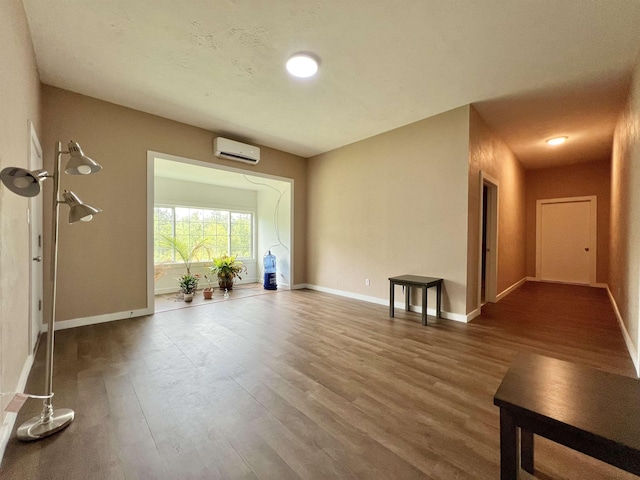 unfurnished living room with a wall mounted AC, baseboards, and wood finished floors