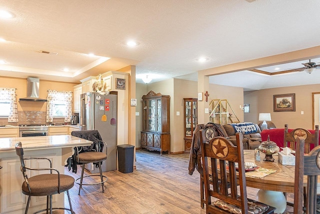 dining space featuring ceiling fan with notable chandelier, light wood-type flooring, a textured ceiling, and a tray ceiling