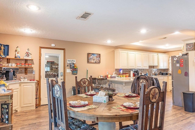 dining space featuring a tray ceiling, sink, light hardwood / wood-style floors, and a textured ceiling