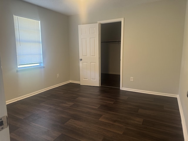 unfurnished bedroom featuring a walk in closet, a closet, and dark wood-type flooring