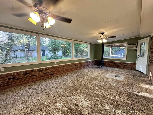 interior space with a wall unit AC, a wood stove, ceiling fan, and brick wall