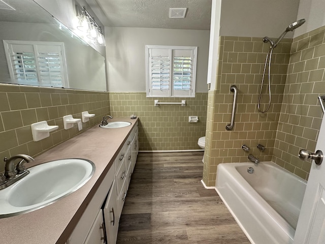 full bathroom with hardwood / wood-style floors, a textured ceiling, toilet, vanity, and tile walls