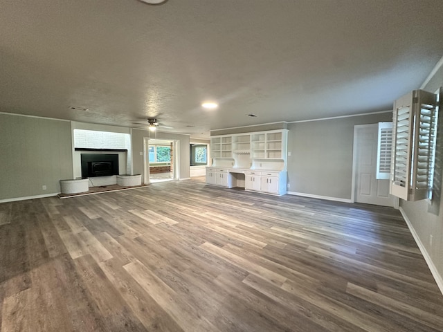 unfurnished living room featuring ceiling fan, built in desk, wood-type flooring, and a textured ceiling