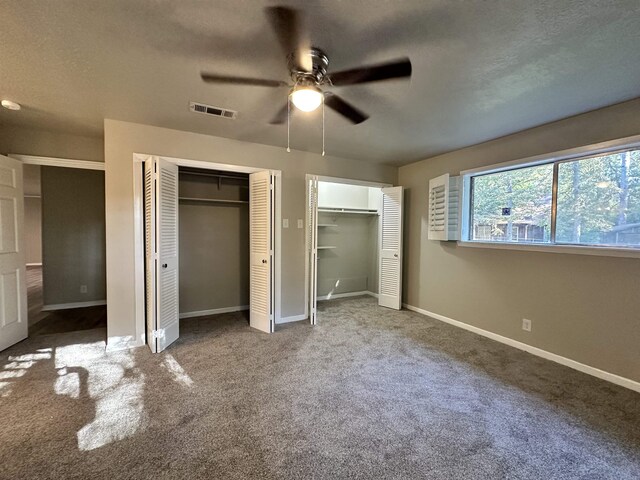 unfurnished bedroom with a textured ceiling, ceiling fan, carpet, and two closets