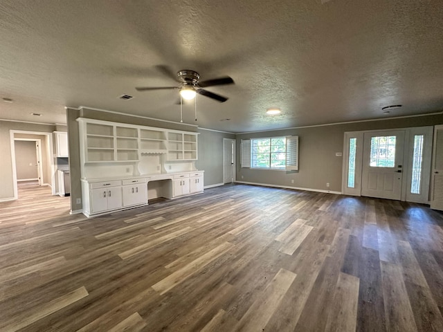 unfurnished living room with dark hardwood / wood-style floors, ceiling fan, built in desk, a textured ceiling, and ornamental molding