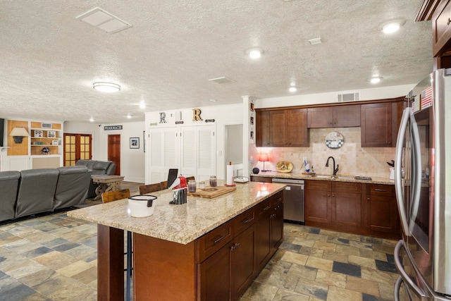 1280 Cherokee Ln, Beaumont, TX 77702 - kitchen featuring stainless steel appliances, a textured ceiling, stone finish floors, a kitchen island, and light stone countertops