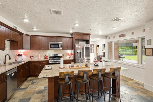 1280 Cherokee Ln, Beaumont, TX 77702 - kitchen with appliances with stainless steel finishes, stone tile flooring, a center island, decorative backsplash, and a textured ceiling