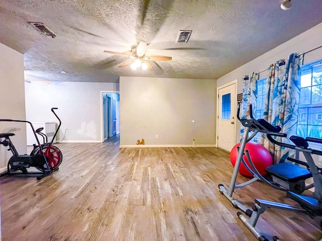 workout room with ceiling fan, wood-type flooring, and a textured ceiling