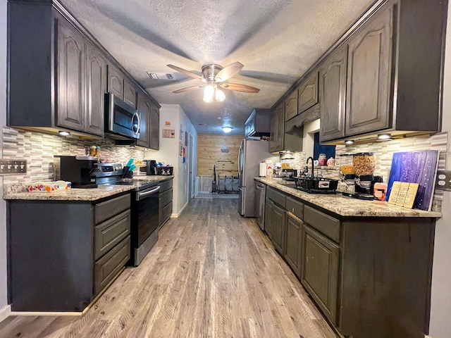 kitchen with ceiling fan, decorative backsplash, a textured ceiling, appliances with stainless steel finishes, and light hardwood / wood-style floors