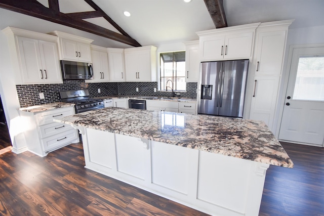 kitchen featuring a sink, light stone counters, tasteful backsplash, appliances with stainless steel finishes, and vaulted ceiling with beams