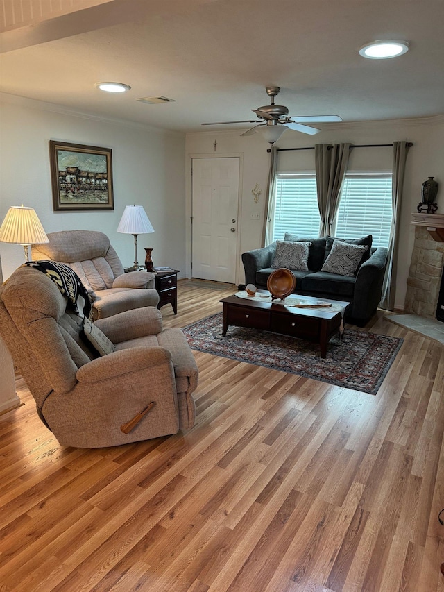 living room with light hardwood / wood-style flooring, ceiling fan, and a stone fireplace