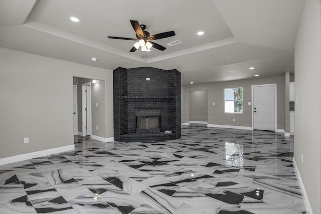 unfurnished living room featuring a brick fireplace, ceiling fan, and a tray ceiling