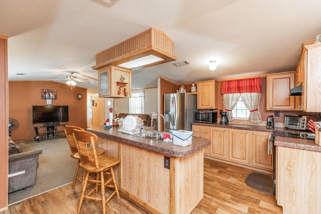 kitchen with light hardwood / wood-style flooring, light brown cabinetry, appliances with stainless steel finishes, kitchen peninsula, and a breakfast bar area