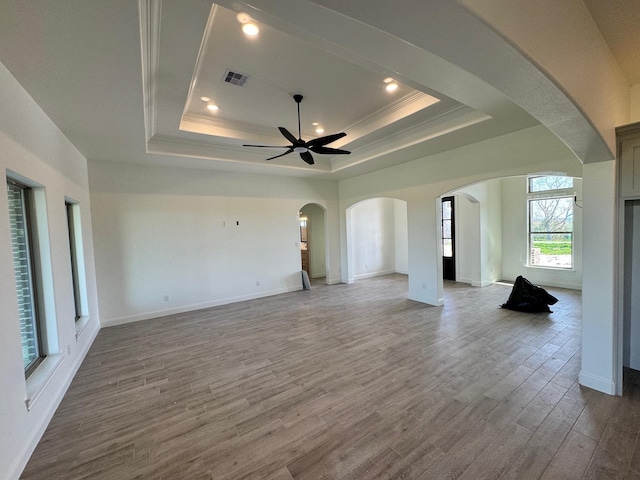 unfurnished living room featuring wood finished floors, crown molding, a ceiling fan, a raised ceiling, and arched walkways