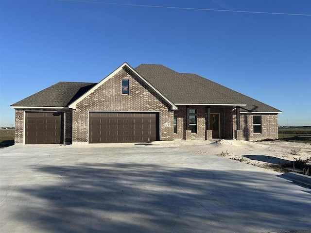 view of front of house with roof with shingles, driveway, brick siding, and a garage