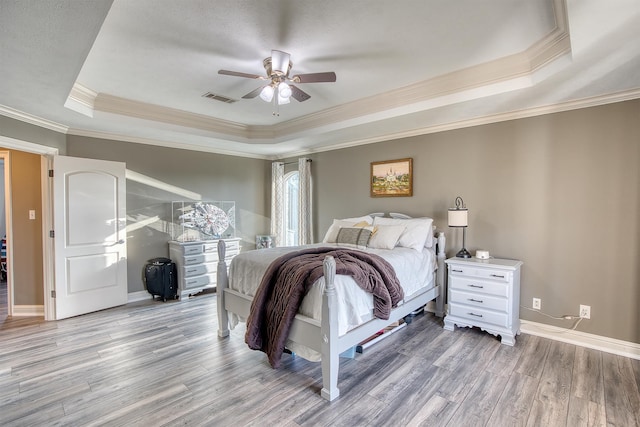 bedroom featuring crown molding, a tray ceiling, light hardwood / wood-style floors, and ceiling fan