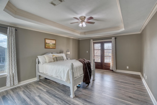 bedroom with french doors, wood-type flooring, ornamental molding, and a tray ceiling