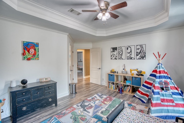 game room with ceiling fan, ornamental molding, a tray ceiling, and light wood-type flooring