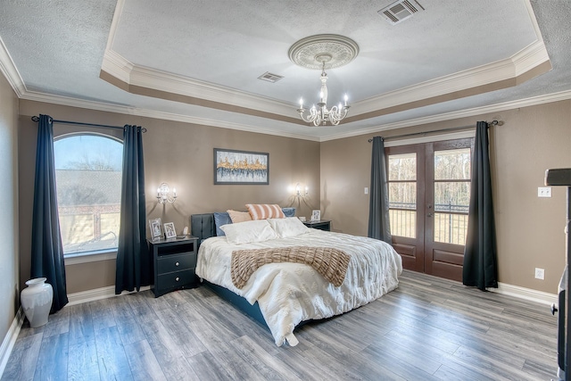 bedroom with hardwood / wood-style flooring, a textured ceiling, access to outside, a raised ceiling, and a chandelier