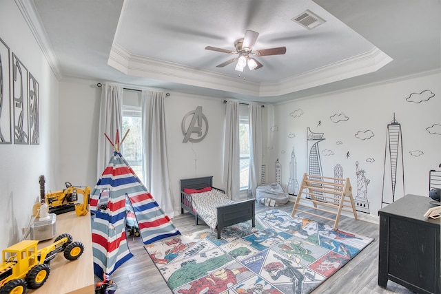 bedroom with ceiling fan, ornamental molding, a raised ceiling, and hardwood / wood-style floors