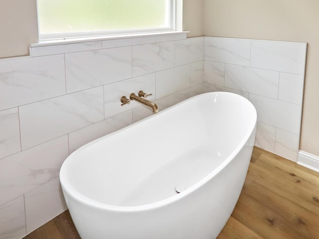 full bath featuring a freestanding tub, tile walls, and wood finished floors