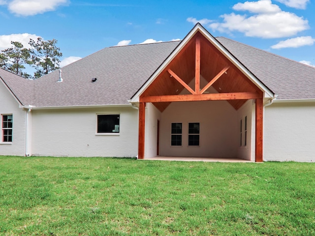 rear view of property with a yard, roof with shingles, and a patio