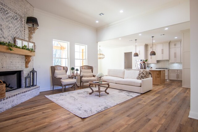 living room with ornamental molding, a brick fireplace, wood finished floors, and visible vents