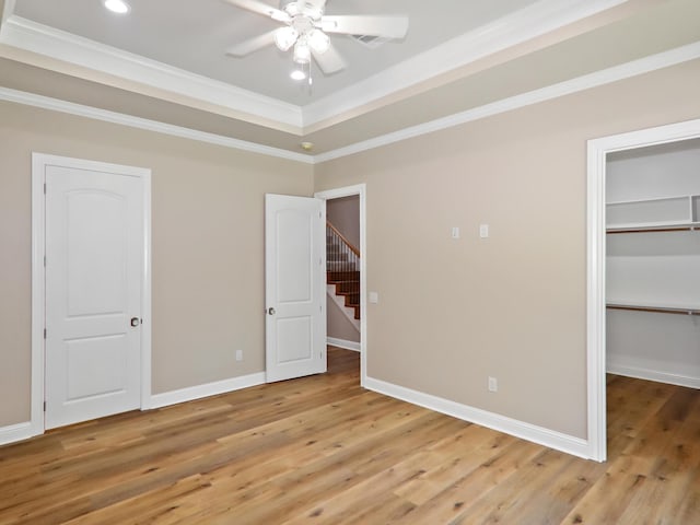 unfurnished bedroom with ornamental molding, a tray ceiling, baseboards, and wood finished floors