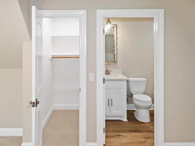 half bath with toilet, vanity, baseboards, and wood finished floors