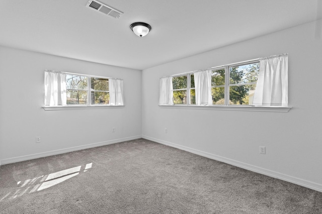 carpeted spare room featuring baseboards, visible vents, and a healthy amount of sunlight