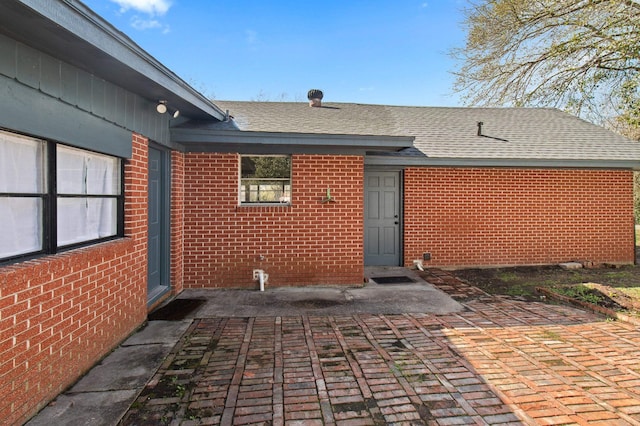 property entrance featuring a shingled roof, a patio area, and brick siding