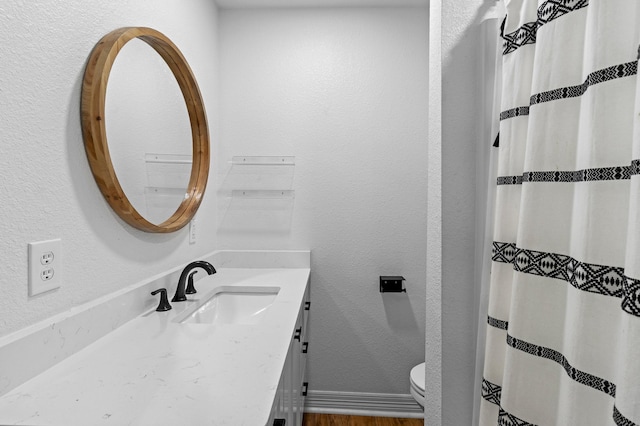 bathroom featuring baseboards, a textured wall, vanity, and toilet