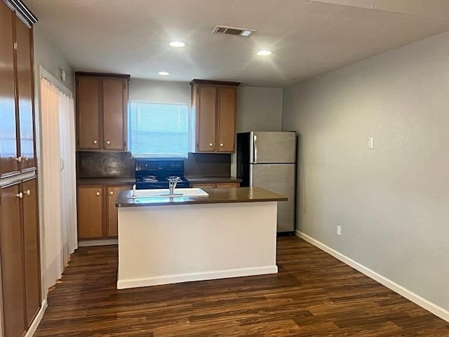 kitchen with visible vents, an island with sink, dark countertops, and freestanding refrigerator