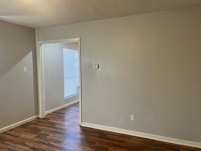 empty room featuring dark wood-style flooring, a textured ceiling, and baseboards