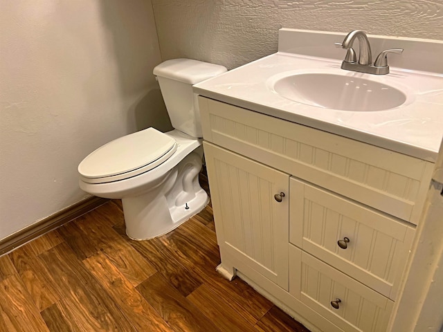 half bathroom with a textured wall, toilet, vanity, wood finished floors, and baseboards