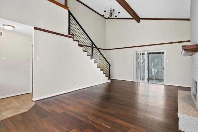 unfurnished living room featuring hardwood / wood-style floors, a towering ceiling, beamed ceiling, and a brick fireplace