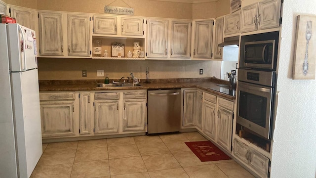 kitchen with light tile patterned floors, under cabinet range hood, stainless steel appliances, a sink, and dark countertops