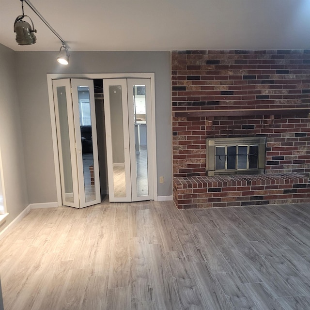 unfurnished living room featuring wood-type flooring and a brick fireplace