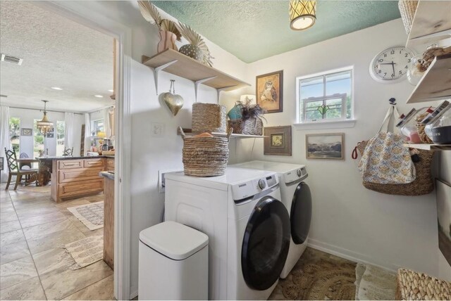 clothes washing area with visible vents, laundry area, a textured ceiling, and washing machine and dryer