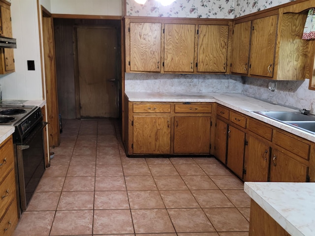 kitchen with range hood, black range, light tile patterned floors, and sink