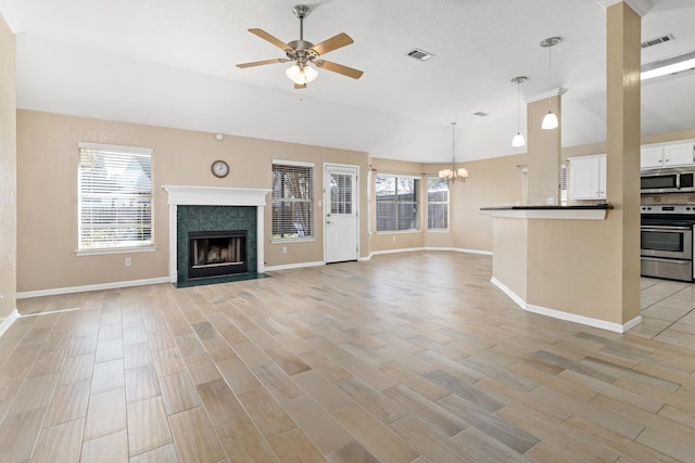 unfurnished living room featuring vaulted ceiling, a premium fireplace, and ceiling fan with notable chandelier