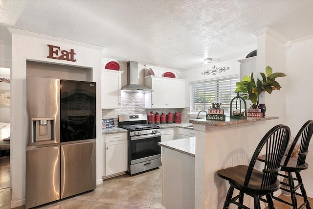 kitchen with white cabinetry, wall chimney exhaust hood, kitchen peninsula, a kitchen bar, and appliances with stainless steel finishes