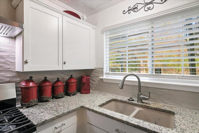 kitchen with light stone countertops, crown molding, sink, range, and white cabinetry