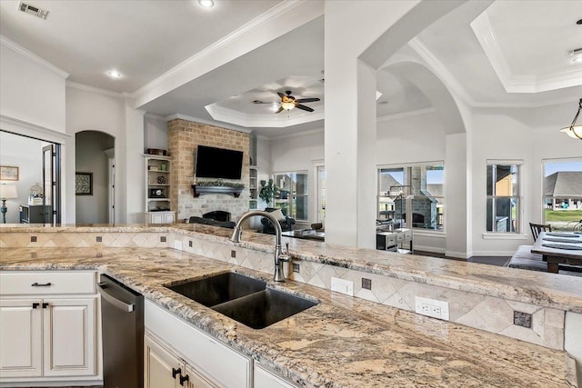 kitchen featuring ceiling fan, sink, a raised ceiling, a fireplace, and white cabinets