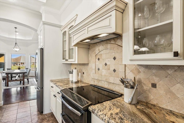 kitchen featuring electric range, hanging light fixtures, premium range hood, dark stone countertops, and decorative backsplash