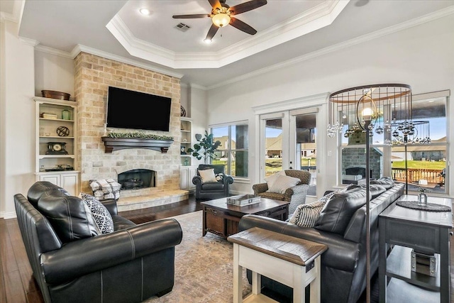 living room with a raised ceiling, hardwood / wood-style floors, a fireplace, ceiling fan with notable chandelier, and ornamental molding