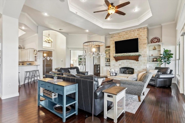 living room featuring dark wood-type flooring, a raised ceiling, crown molding, ceiling fan, and a fireplace