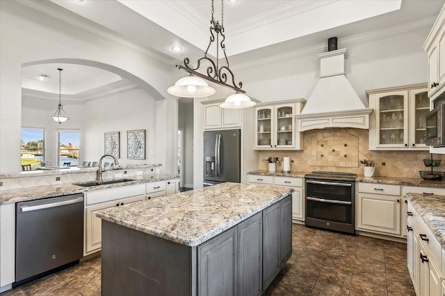 kitchen featuring premium range hood, stainless steel appliances, a raised ceiling, pendant lighting, and a center island