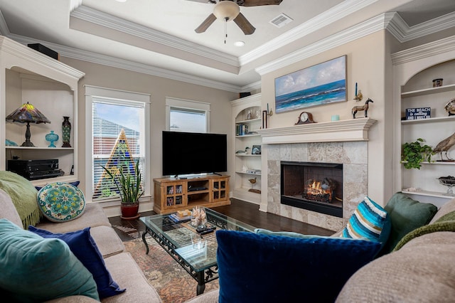 living area featuring a tray ceiling, built in shelves, wood finished floors, and visible vents